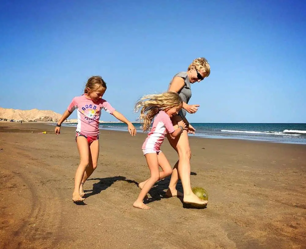 mom and two kids kicking a ball around on the beach