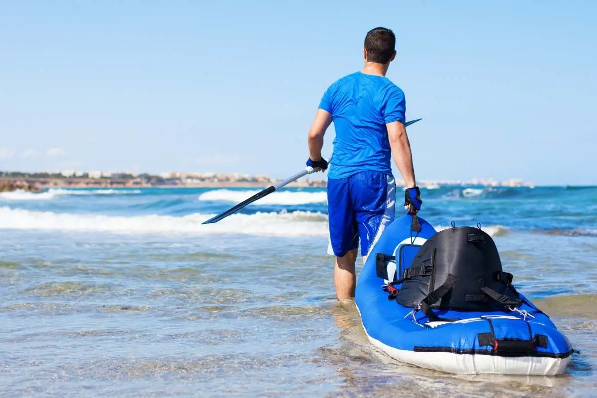 man carrying an inflatable kayak into the water.